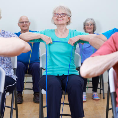 Group of people seated on chairs performing resistance band exercises in a fitness class setting.