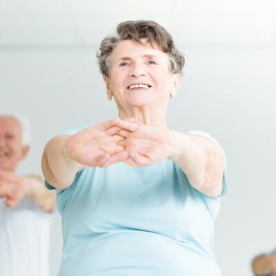 Group of people participating in a seated exercise class, stretching arms forward in a bright indoor fitness studio.