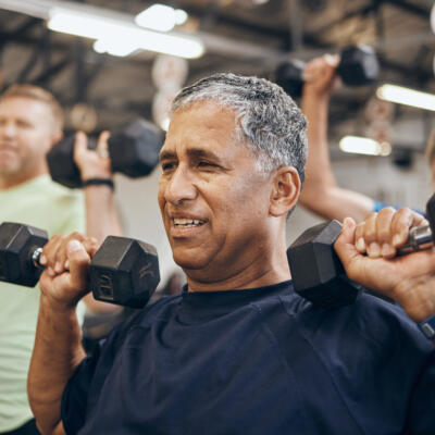 Group of people lifting dumbbells during a strength training class in a gym setting.