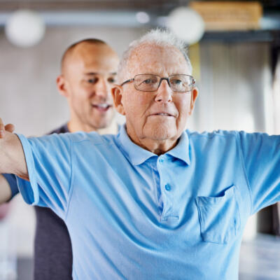 Instructor assisting an older adult with a lateral arm raise using a small dumbbell during exercise.
