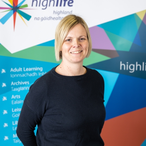 A blonde woman in a black shirt smiles at the camera.