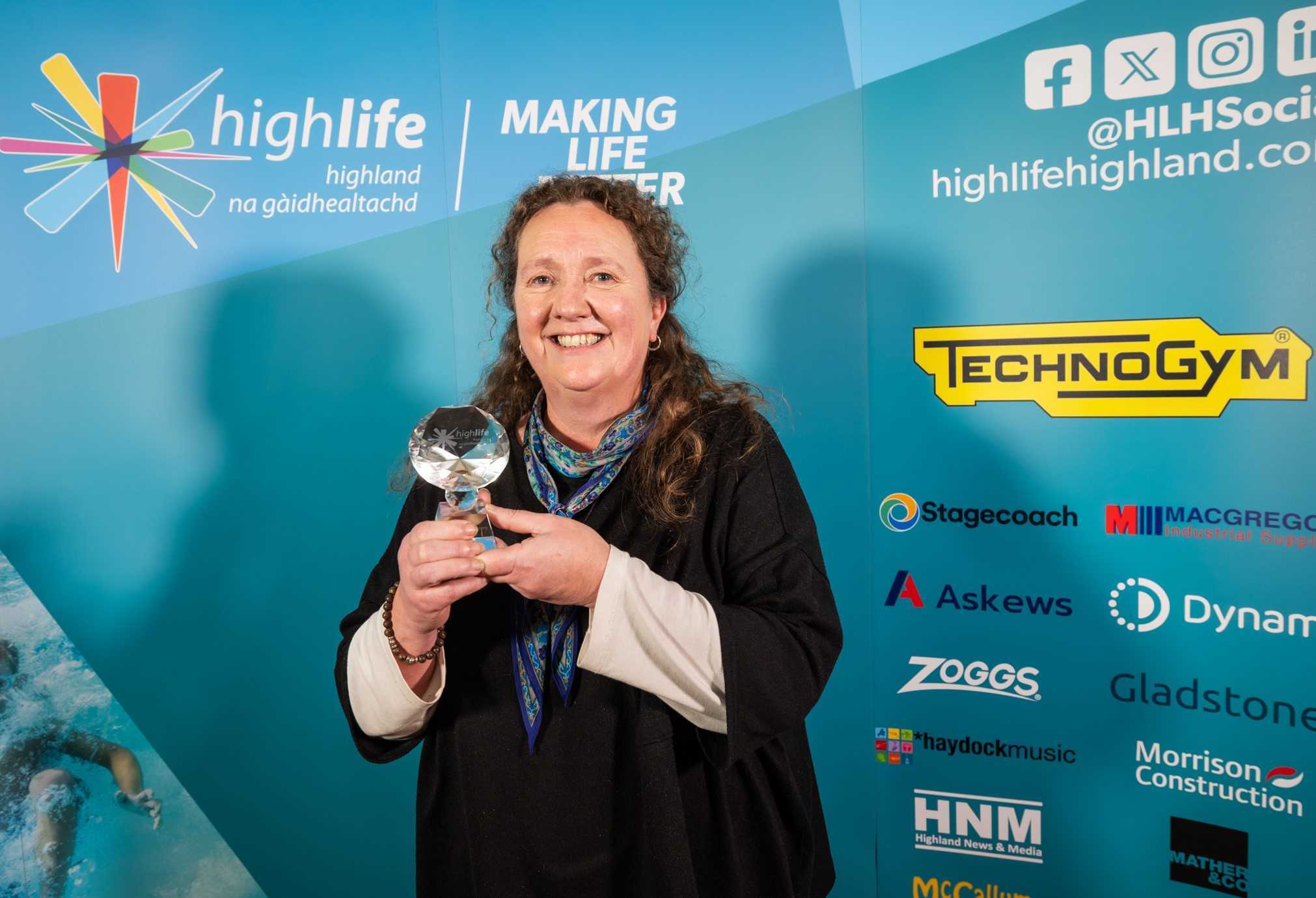 A person holding a glass award in front of a High Life Highland branded backdrop.