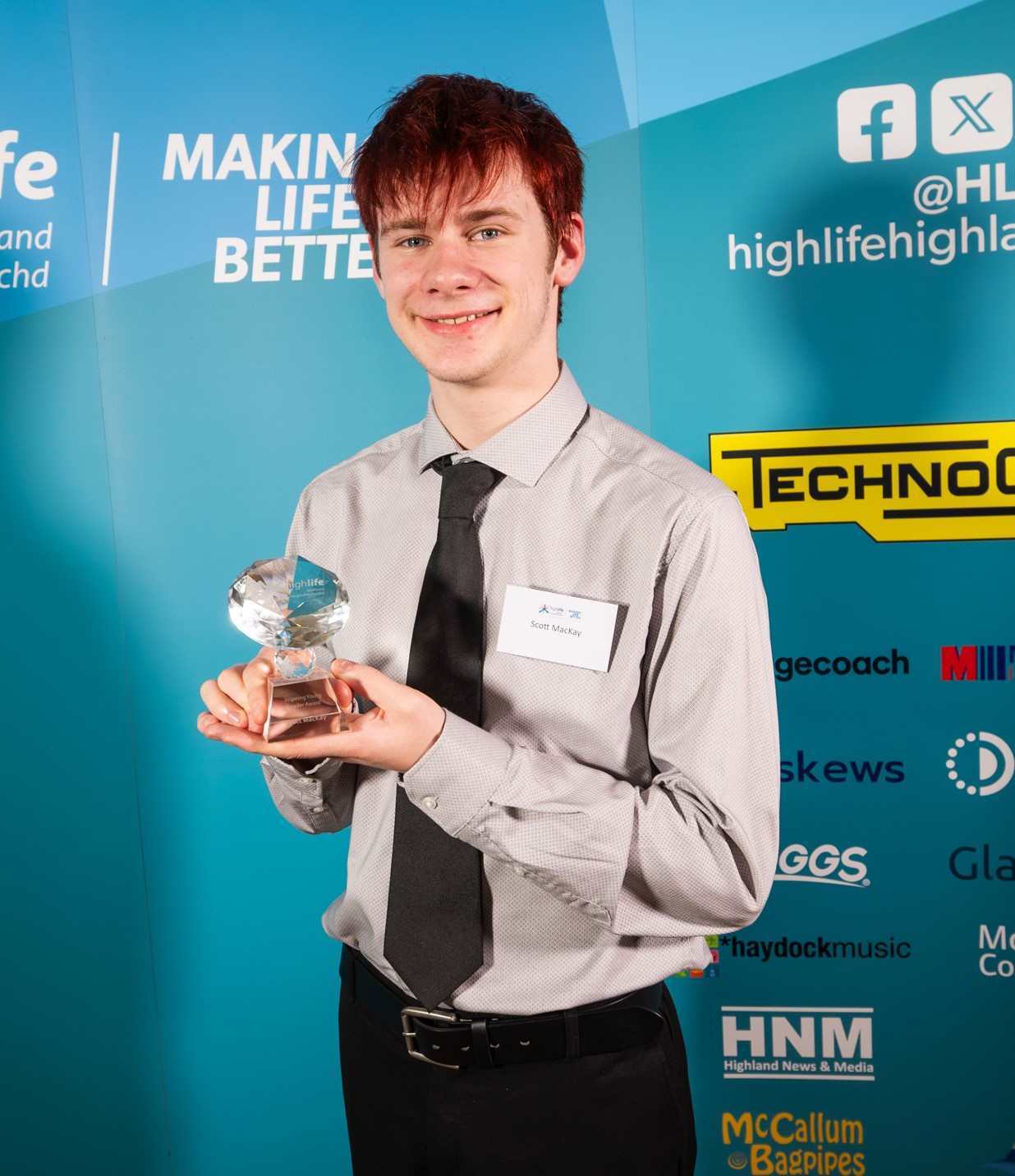 A person holding a glass award in front of a High Life Highland backdrop at an awards event.