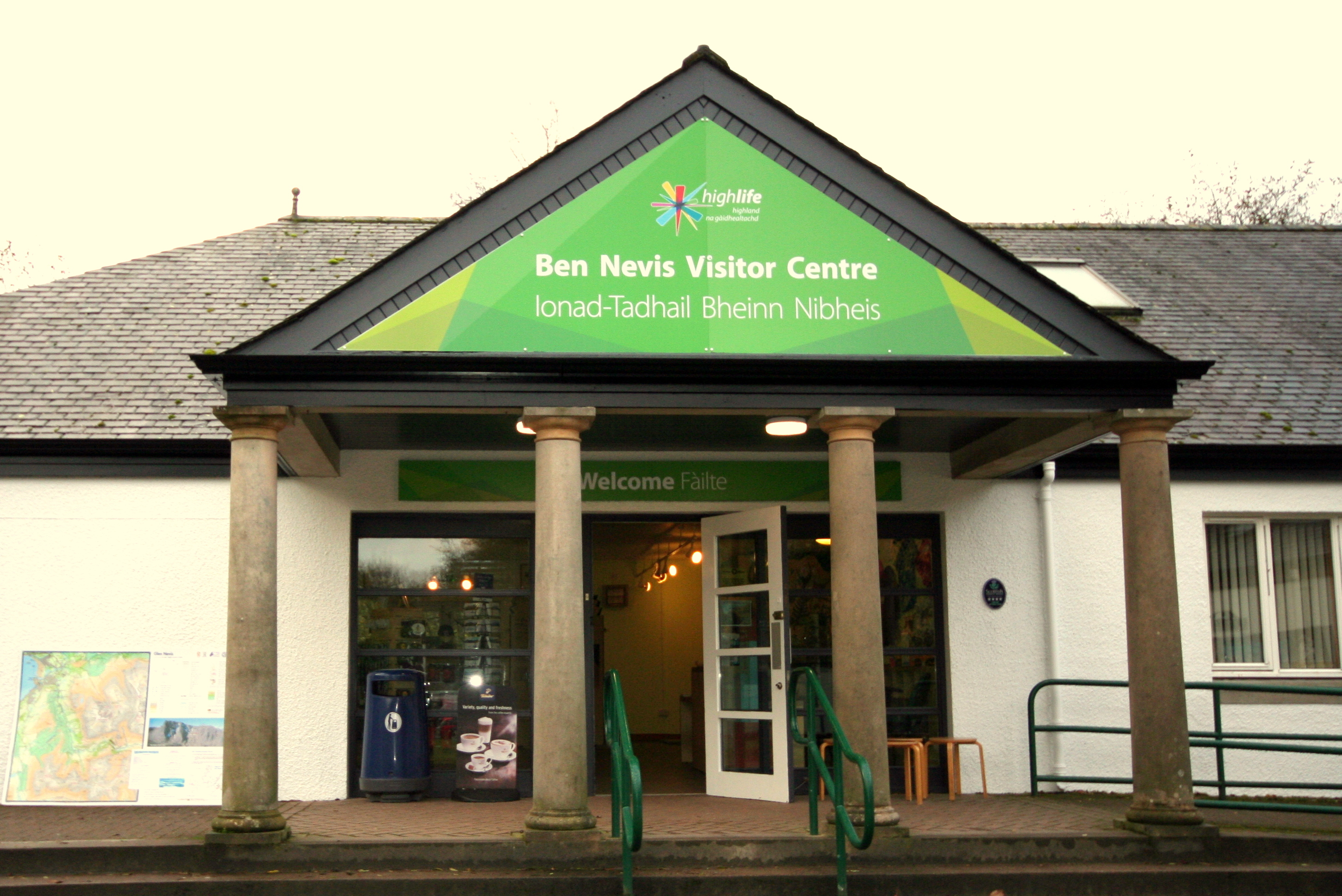 Entrance of Ben Nevis Visitor Centre with green sign and open door.
