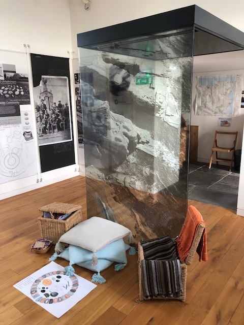 A museum seating area with cushions and baskets beside a large mirrored display column.