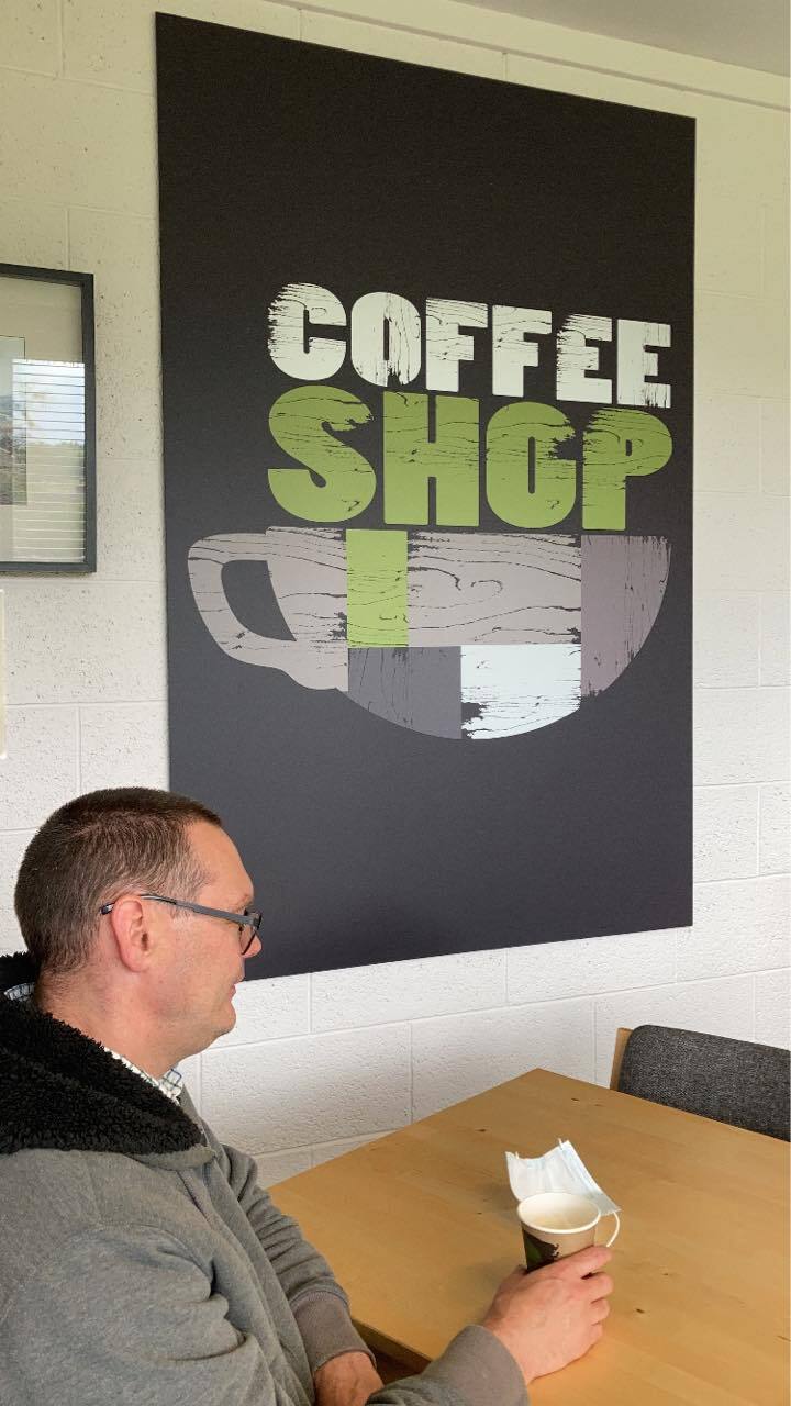 Coffee shop sign on a wall above a table with a cup of coffee