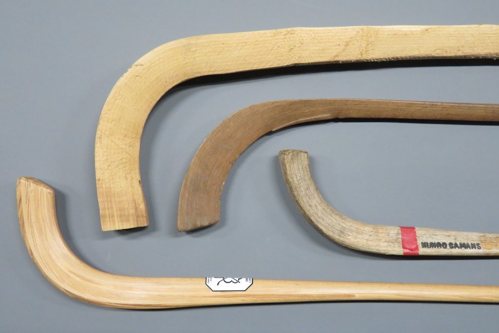 Four different camans displayed side by side, showing variation in wood type, shape and construction.