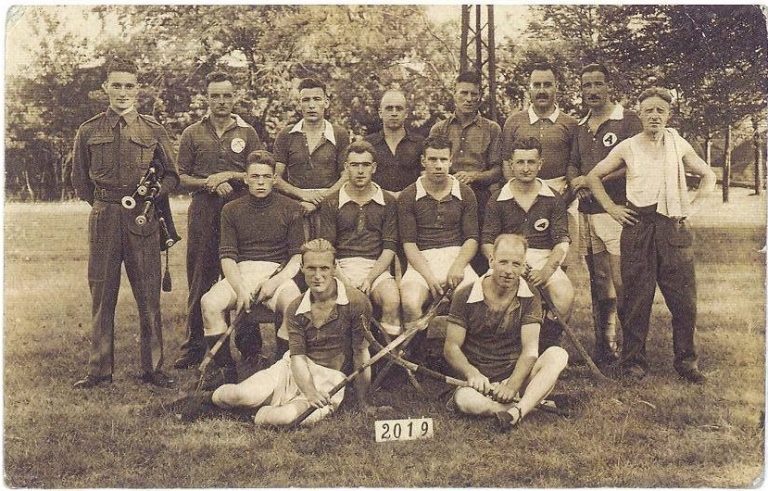 A group photograph of men in sports kit holding shinty sticks at a prisoner of war camp.
