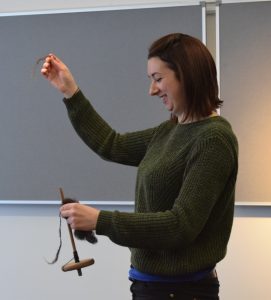 A person holding a drop spindle and a length of spun yarn.