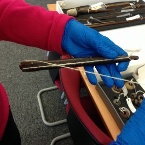 A person wearing blue gloves holding a wooden spindle wrapped with white yarn.