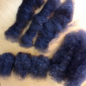 Several dark wool rolags laid out on a wooden table.