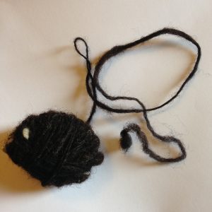 A small ball of dark hand-spun yarn with a loose strand attached.