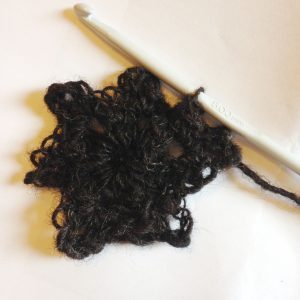 A crocheted star made from dark hand-spun wool with a crochet hook beside it.