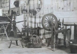 A display of spinning wheels and textile tools arranged against a wooden wall.