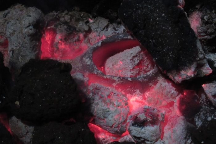 Close‑up of glowing embers with a clay pot heated among the coals.