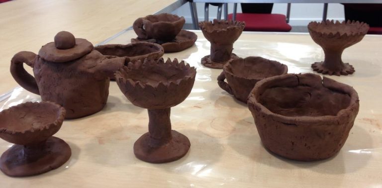 A table full of small handmade clay pots, cups and bowls.