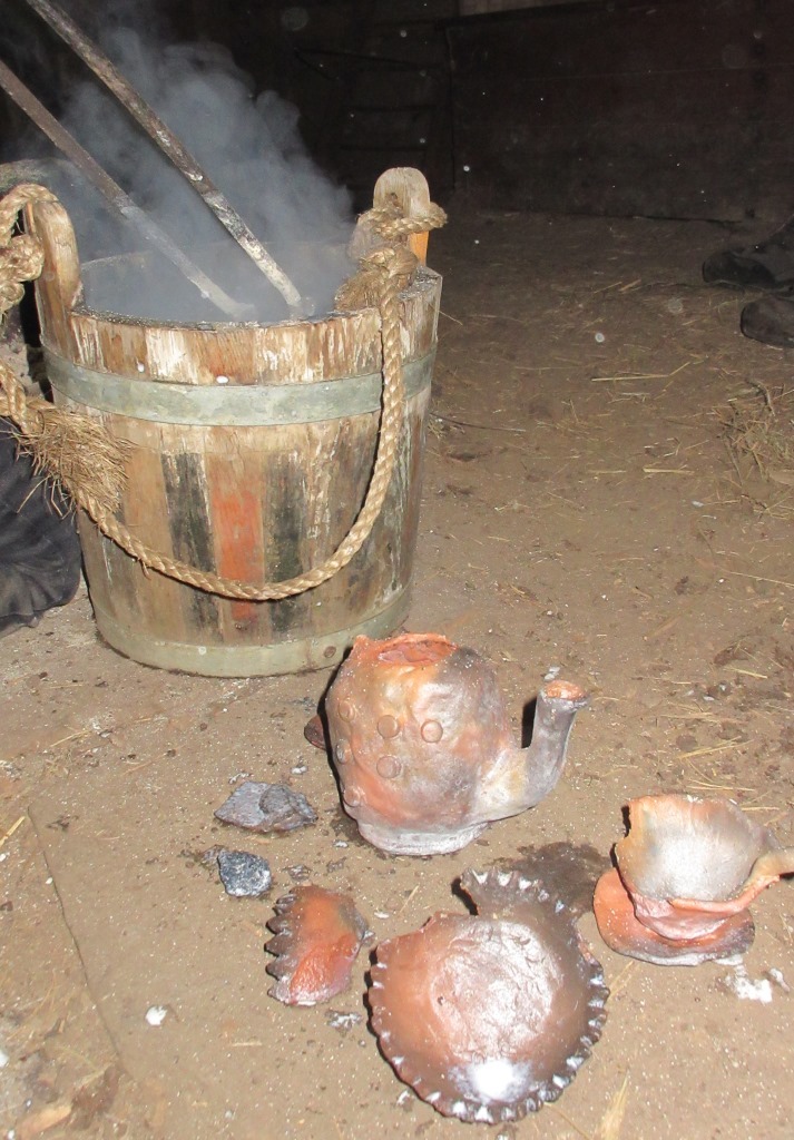 Several fired clay pots placed beside a wooden bucket with rising steam.