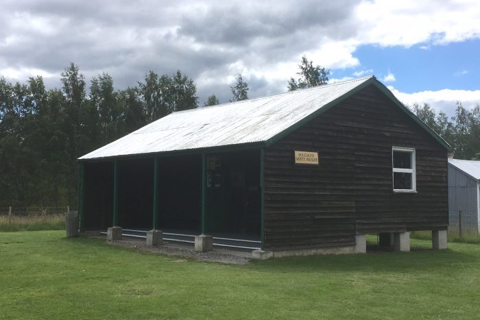 The Boleskine shinty pavilion, a wooden sports building with a metal roof, set on a grassy field.