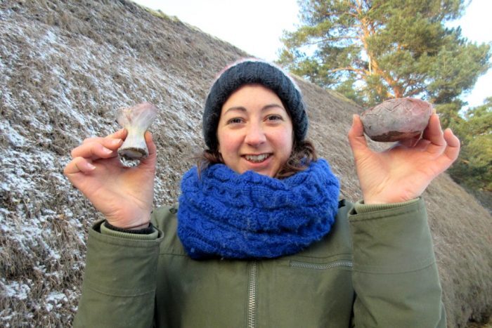A person outdoors holding two small fired clay pots up in each hand.