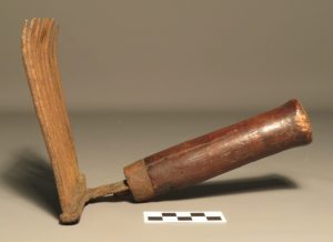 A wooden tool with a curved metal comb and a thick wooden handle.