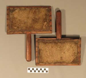 Two wooden hand carders with worn, textured surfaces and short handles.