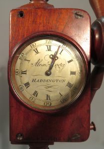 A close‑up of a round clock face set into a wooden textile tool.