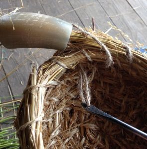 A close-up of a straw basket being stitched together using an awl and a horn funnel.