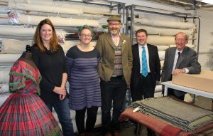 A group of five people standing in a museum storage room beside shelves of rolled textiles and a tartan dress display.