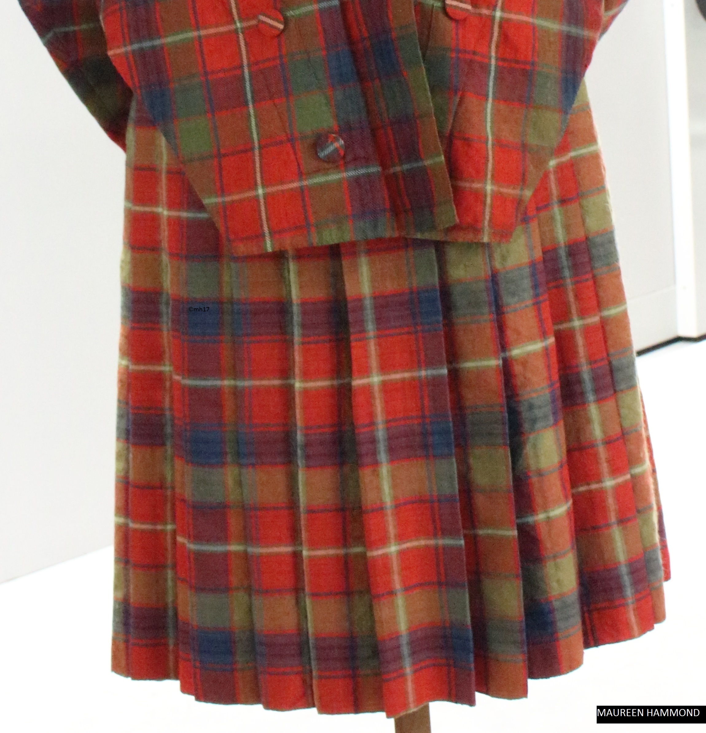 A red, green and blue tartan pleated skirt displayed on a mannequin, shown from the back.