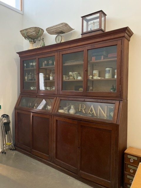 A tall wooden display cabinet with glass doors, containing old medicine bottles and chemist items.