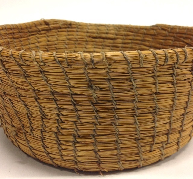 A small round basket made from tightly coiled natural fibres with visible stitching.