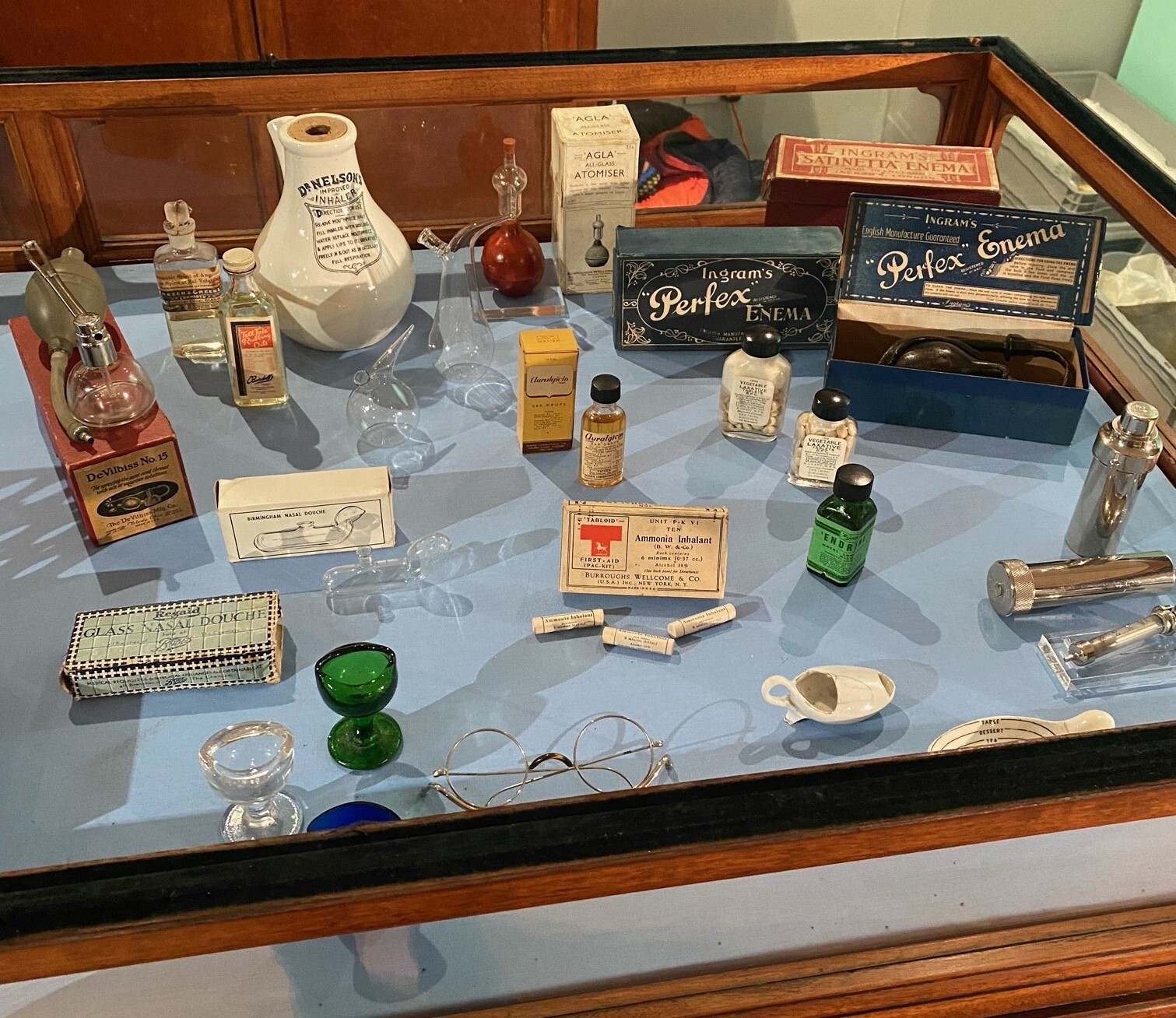 A glass display case containing various historic medical items, including bottles, boxes, glasses and instruments.