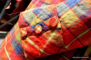 A close‑up view of a red, green and blue tartan jacket showing three covered buttons on the front panel.