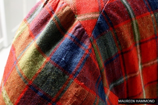 A close‑up of a tartan jacket’s shoulder and upper sleeve, showing the vibrant woven pattern.