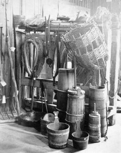A collection of old wooden tools and containers, including churns, buckets, and a large basket hanging on a rack.
