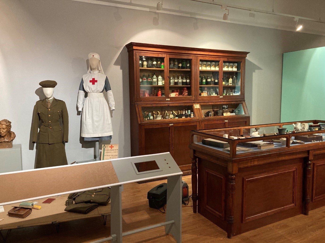 A display area with two mannequins in historic uniforms and a large wooden pharmacy cabinet filled with bottles and medical items.