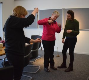 Three people practising spinning with drop spindles in a room.