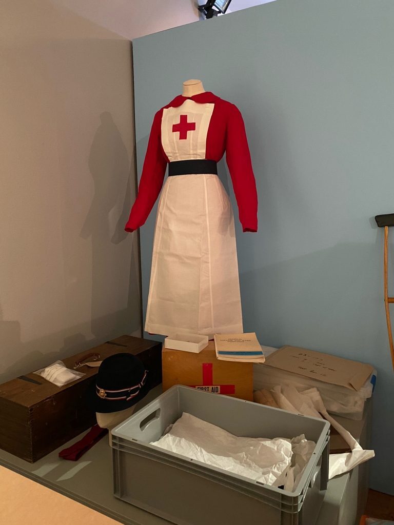 A mannequin dressed in a red and white nurse uniform standing beside boxes and a grey crate with packing materials.