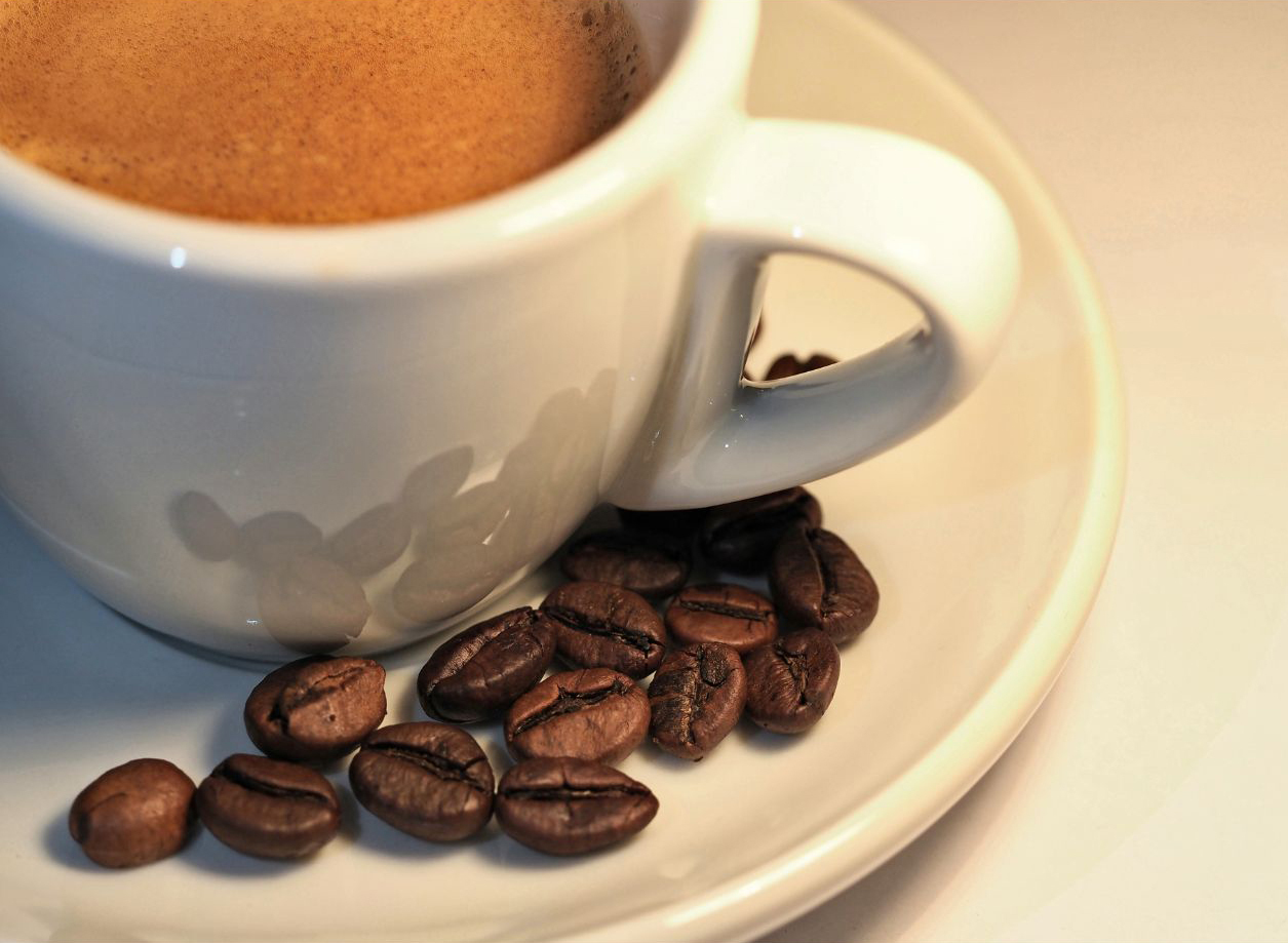 Cup of coffee sitting on a saucer, with some loose coffee beans