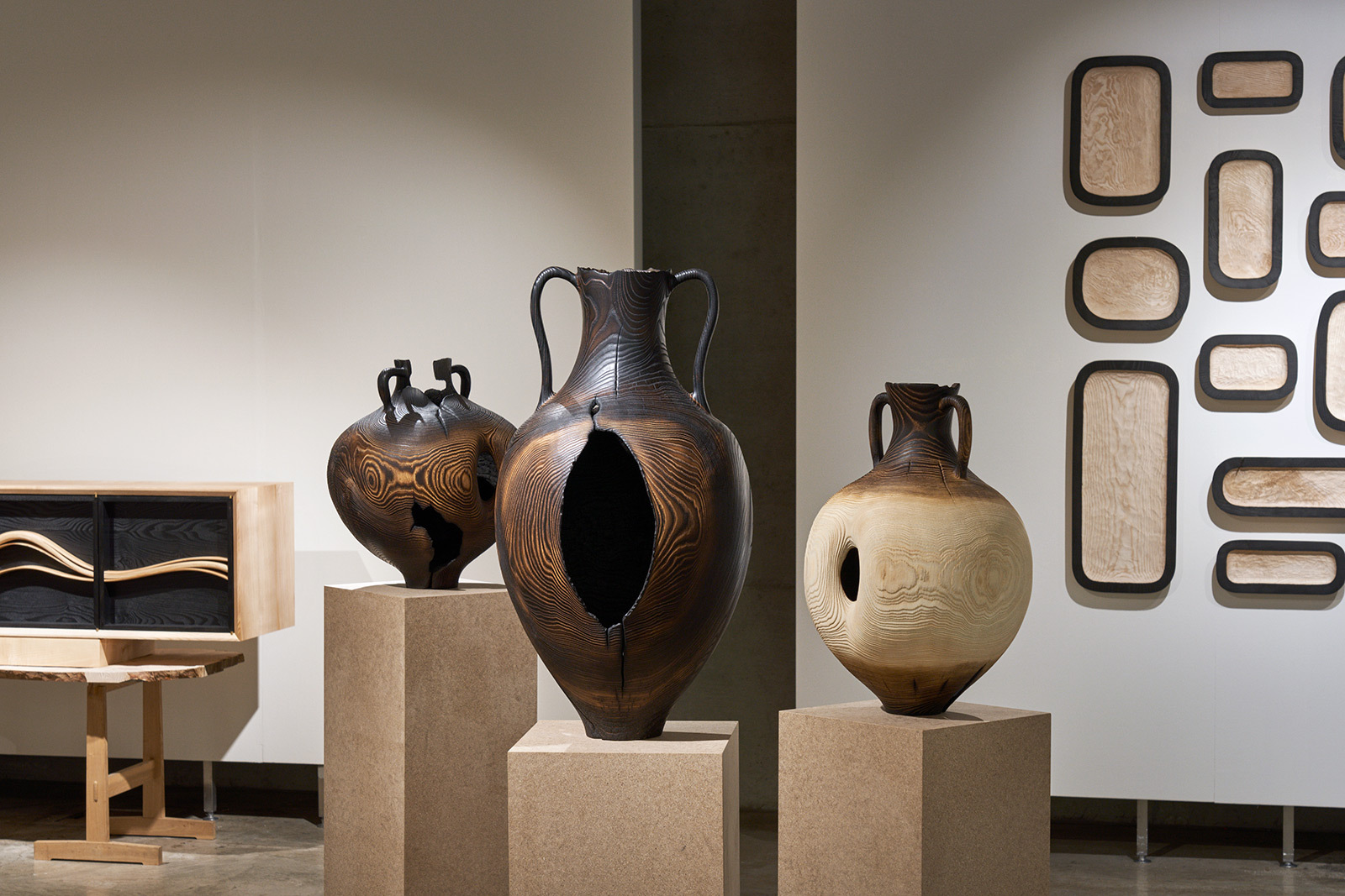 A display of three pots made from wood, placed on three wooden plinths, in an art gallery setting.