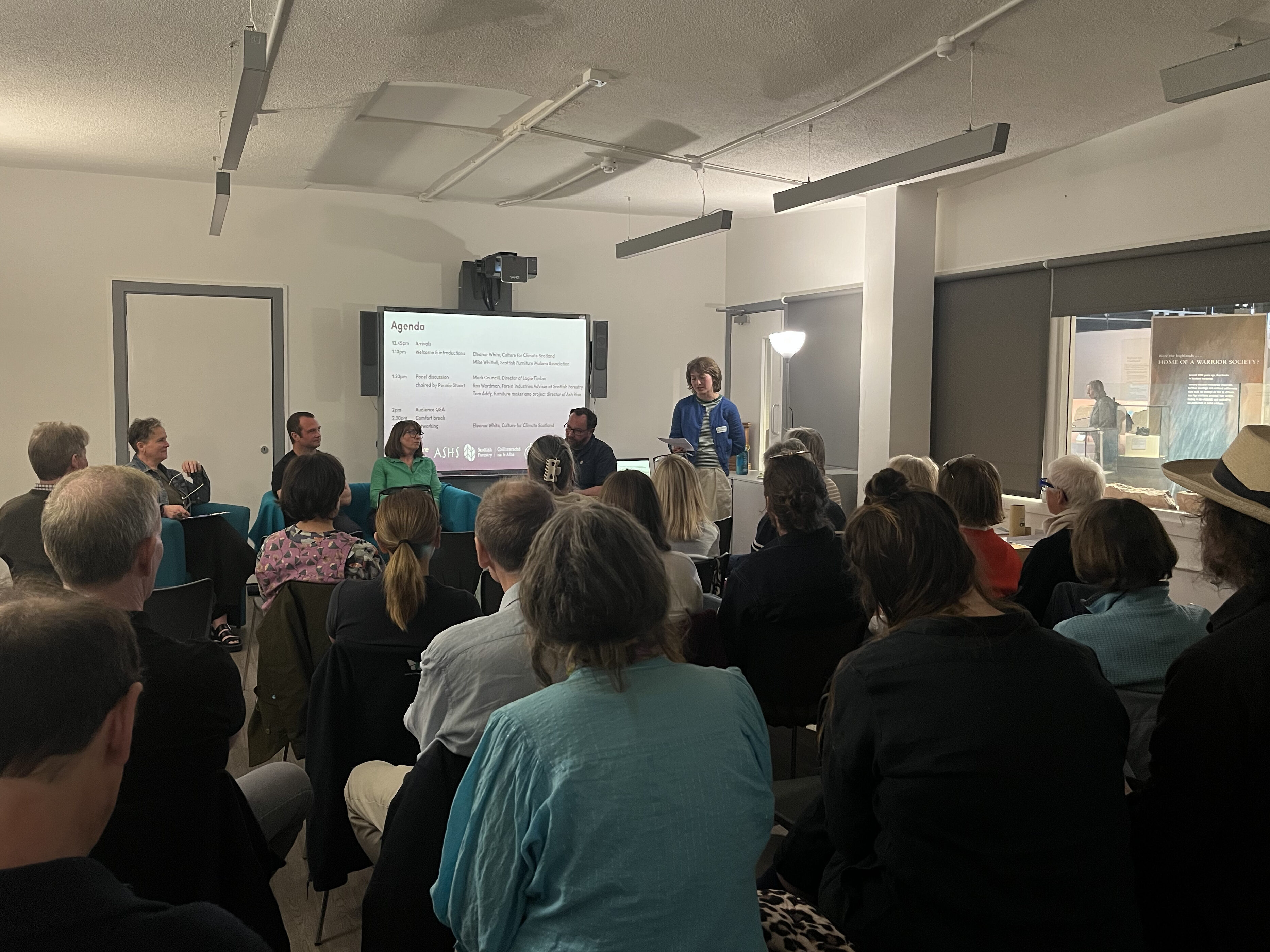 A room full of people sitting no chairs facing a projection screen
