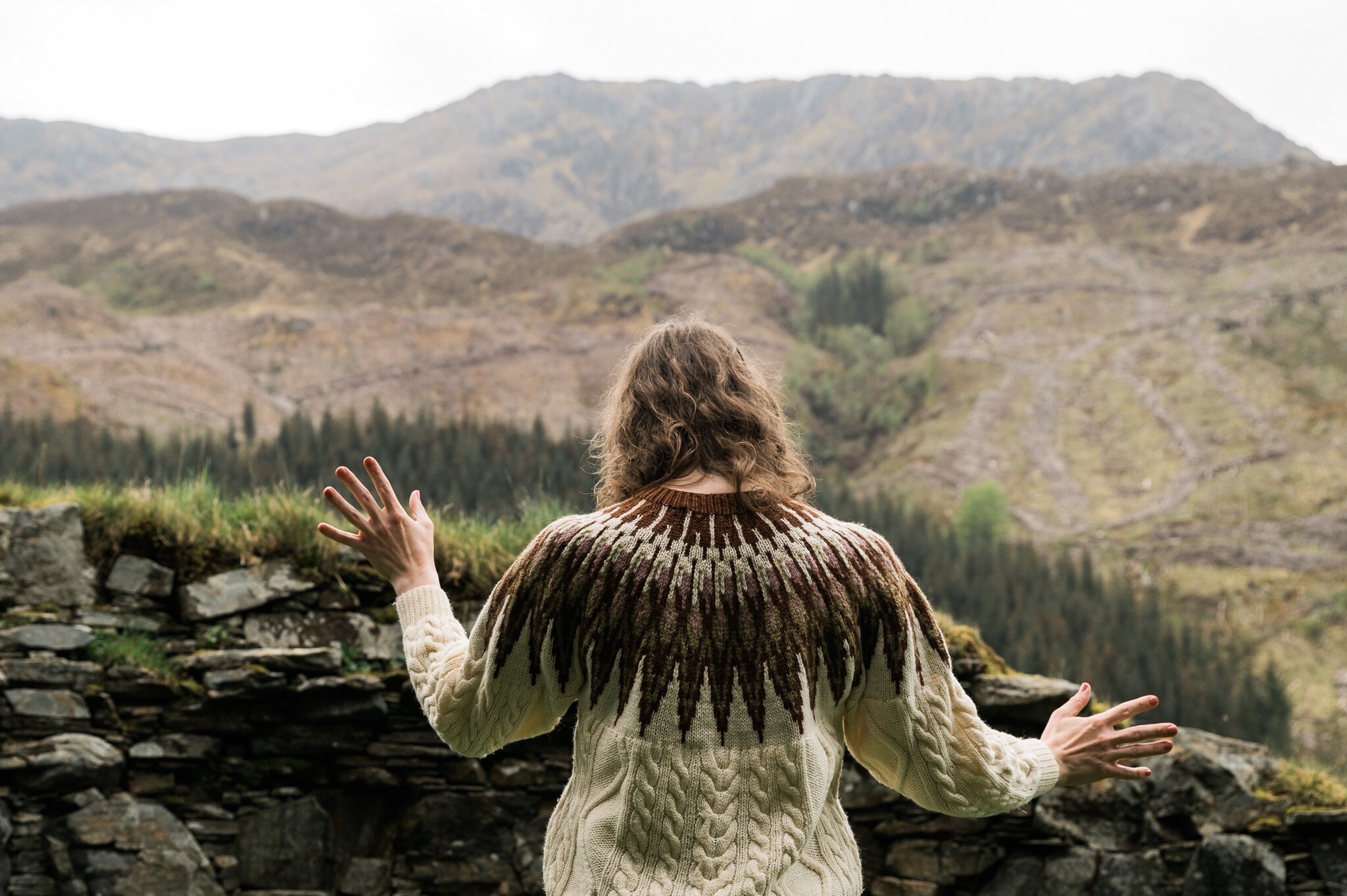 An image of the back of person wearing a woollen jumper and looking out onto an empty Scottish landscape