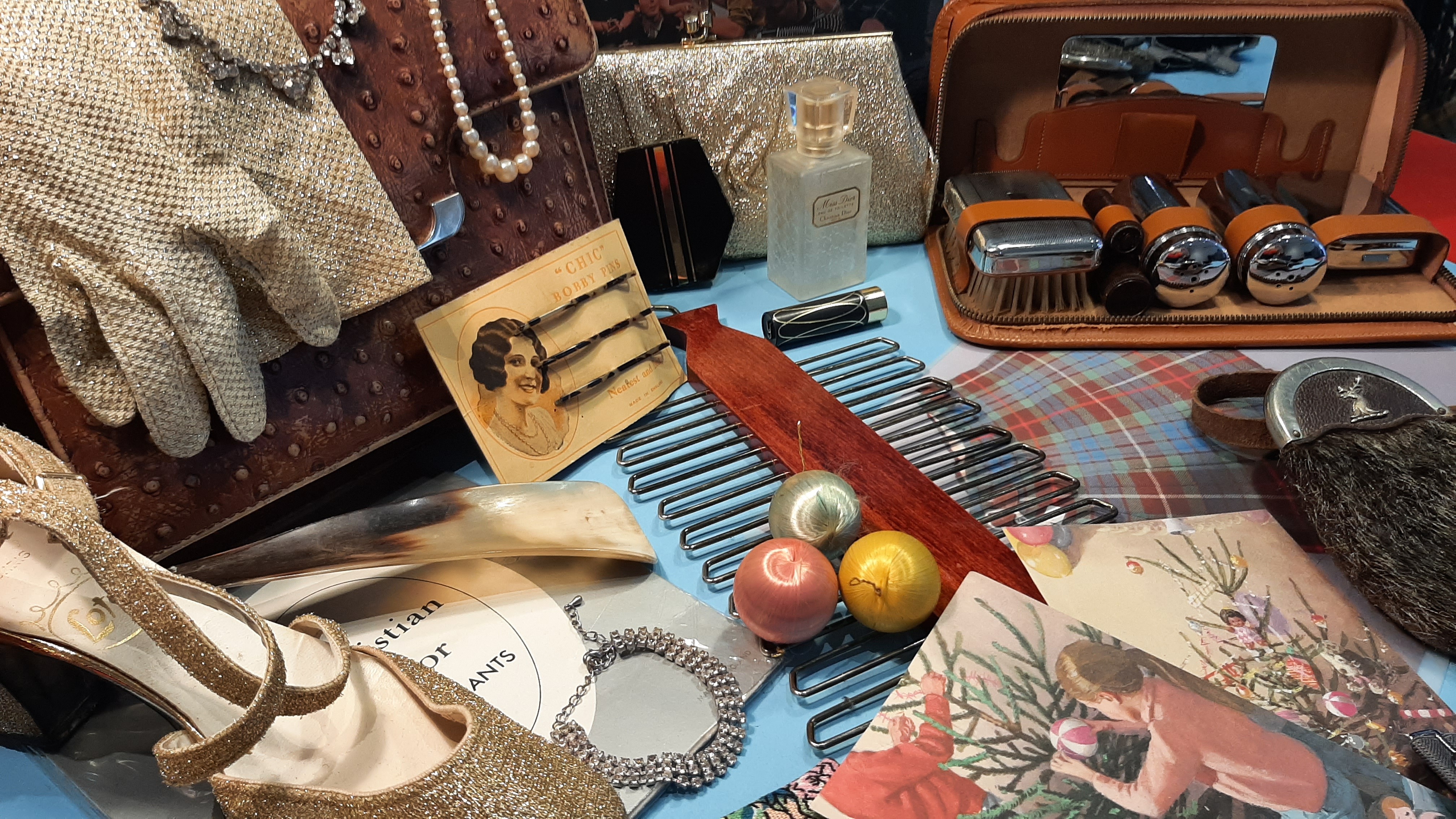 A display of vintage accessories including gloves, jewellery, hair combs, cosmetics, shoes, and grooming tools arranged on a table.
