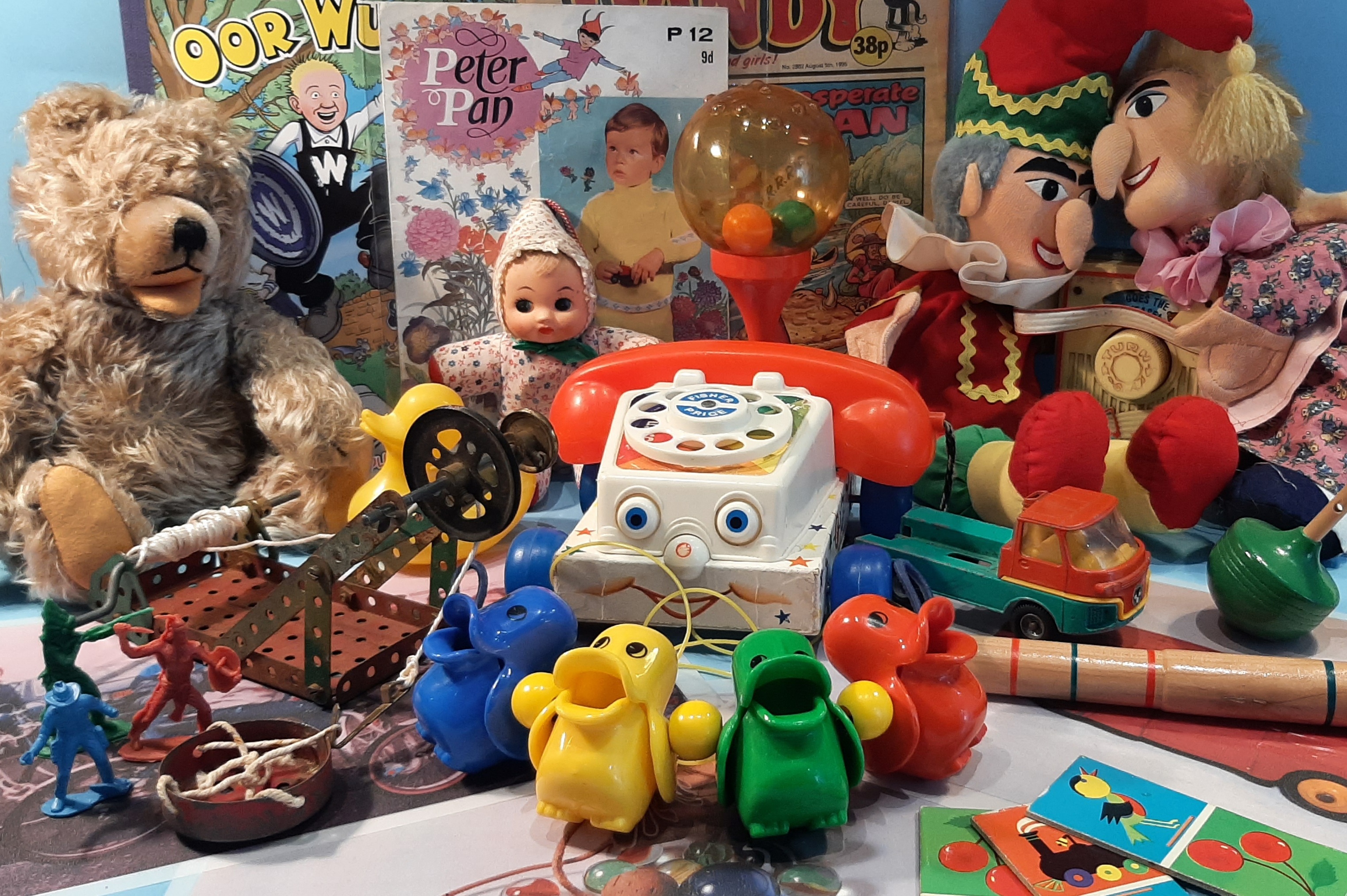 A colourful collection of vintage toys, including a teddy bear, puppets, a toy telephone on wheels, plastic animal figures, a spinning top, and old children’s books arranged together.