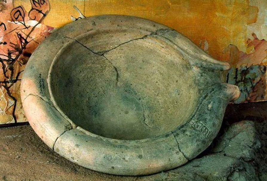 A large, round stone basin with a thick rim and visible cracks, set against a textured background.