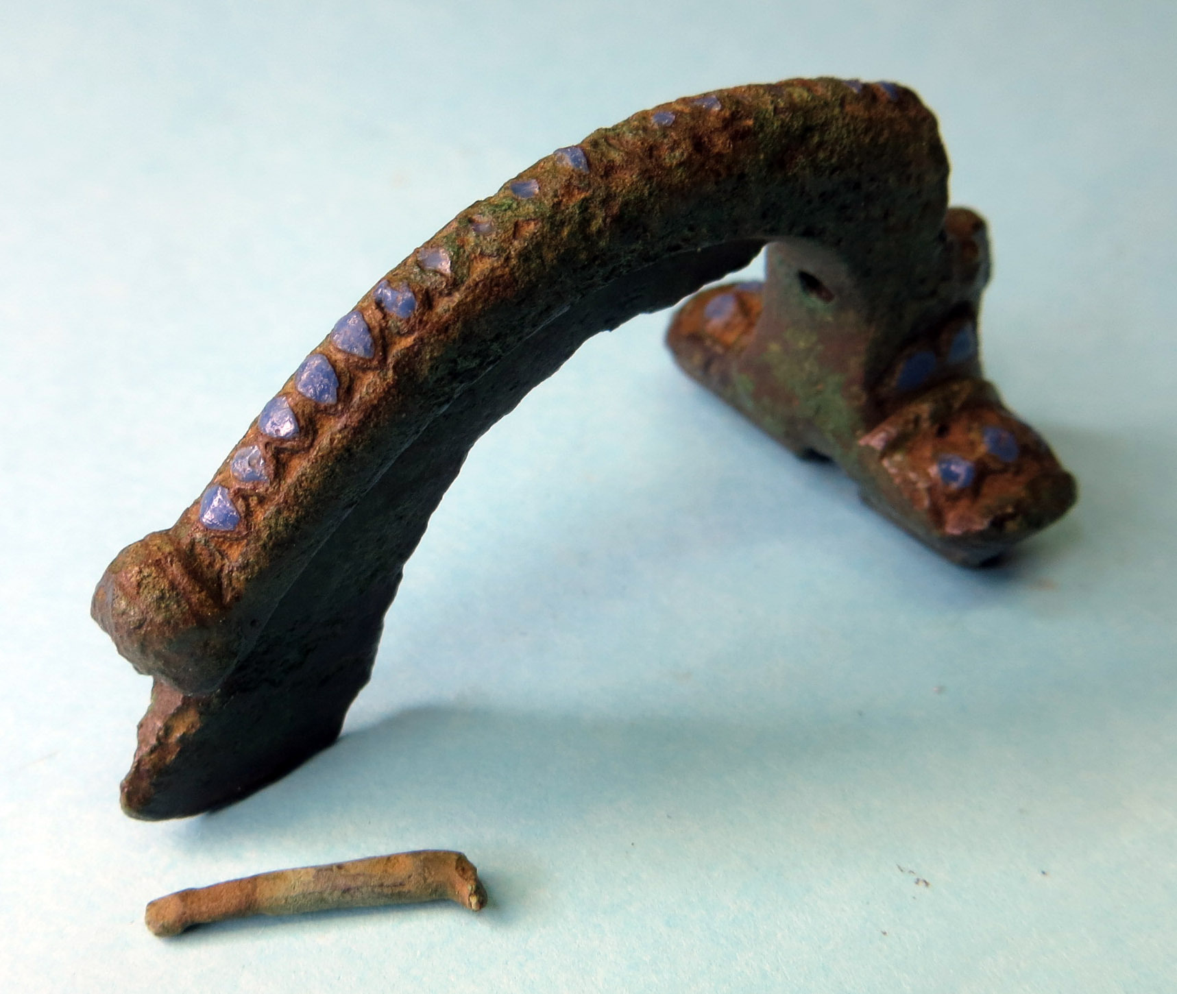 A Roman fibula brooch, which is a long, arched type of metal brooch.  It is missing its pin.  Shown after conservation cleaning, where the bronze metal and coloured enamel decoration can now be seen.