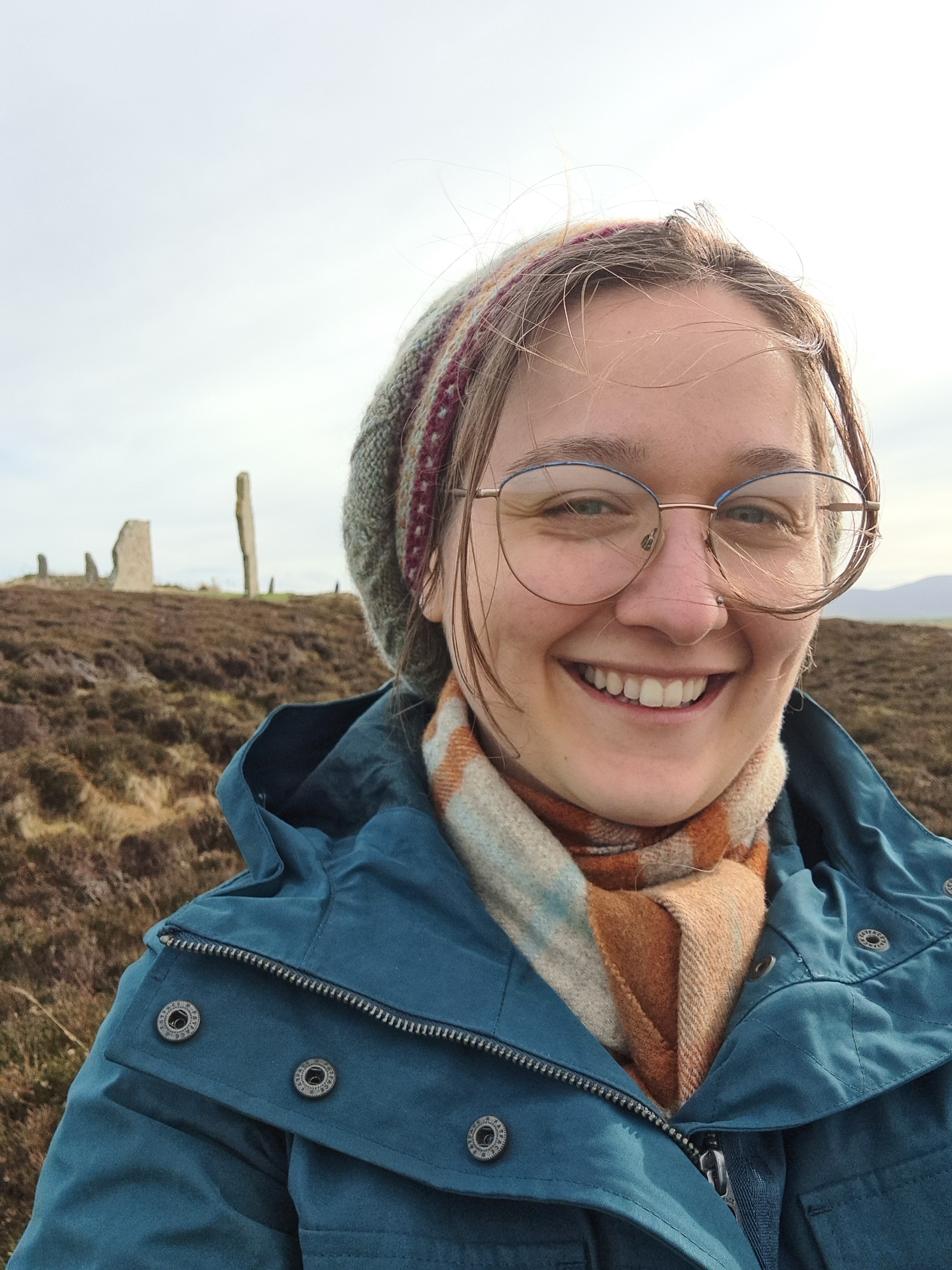 Portrait photograph of PhD candidate, Nysa Loudon, shown outdoors with ancient standing stones in the background.  Image courtesy of Nysa N. Loudon.