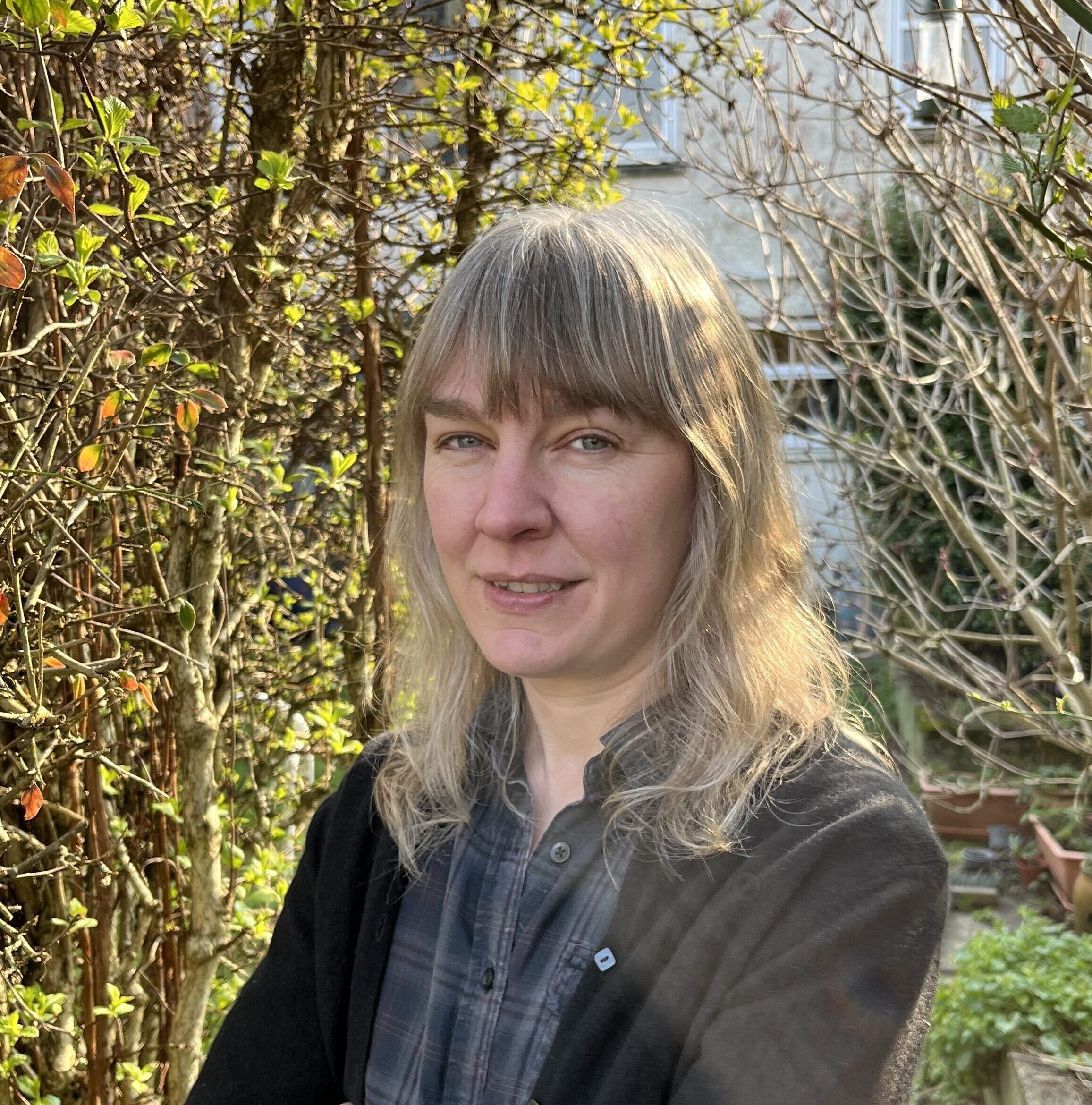 Portrait photograph of Inverness author, Jennifer Morag Henderson, shown standing outdoors with foliage in the background.  Image courtesy of Jennifer Morag Henderson.