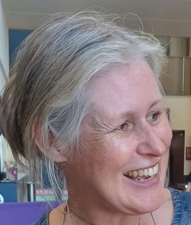Portrait photograph of historian Dr Rhona Ramsay, showing her smiling and looking away from the camera, with an interior in the background.  Image supplied by Dr Rhona Ramsay.