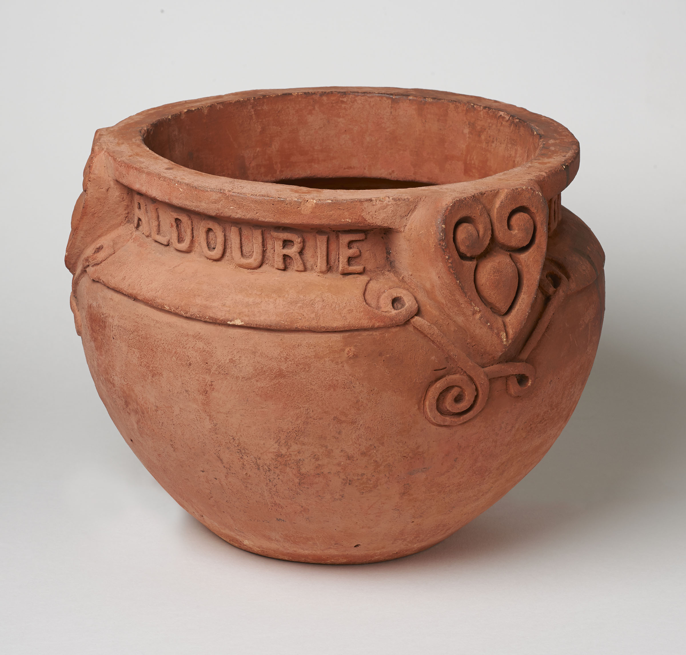 A round terracotta garden pot with three heart-shaped handles fixed around the rim and an inscription running between the handles.